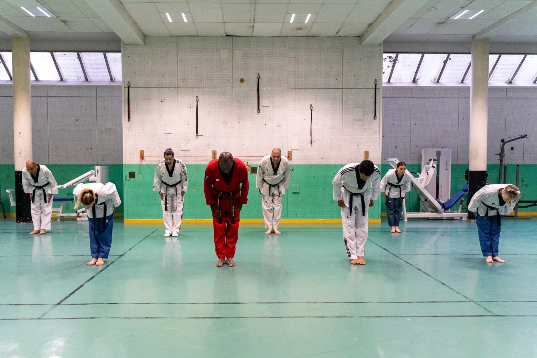 Le groupe adultes salue, ceintures noires en dobok blanc, l'instructeur en dobok rouge au centre