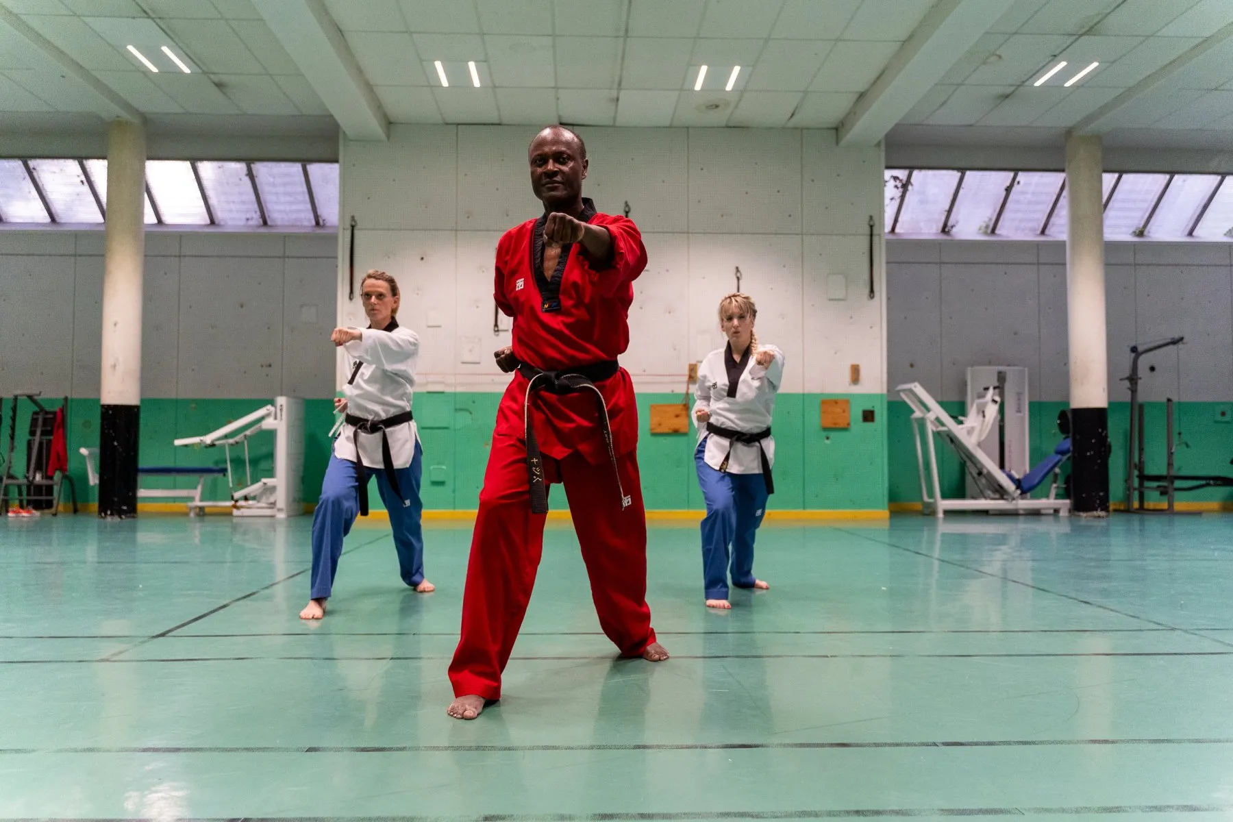 Poomsae à trois – l'instructeur en dobok rouge devant deux ceintures noires, coup de poing de face