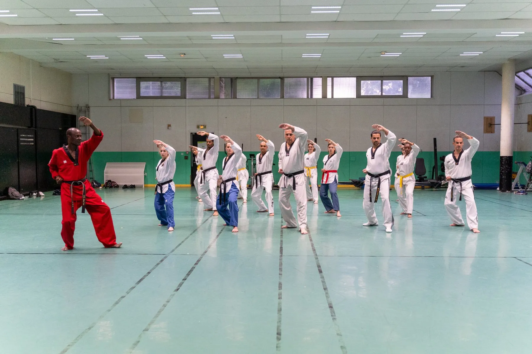 Cours adultes au complet – blocage haut à l'unisson, l'instructeur en dobok rouge devant le groupe