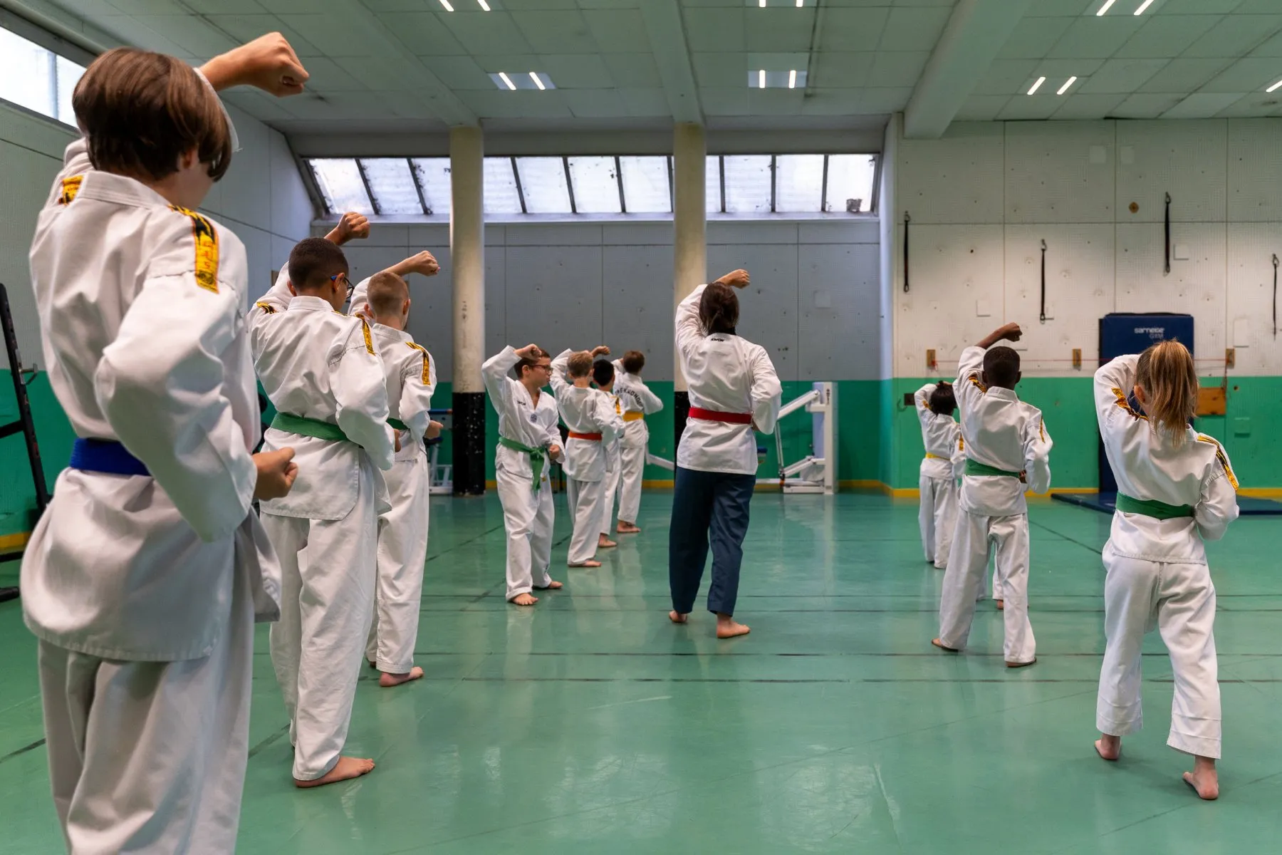 Cours enfants – les élèves répètent un blocage haut, l'instructrice en ceinture rouge au centre